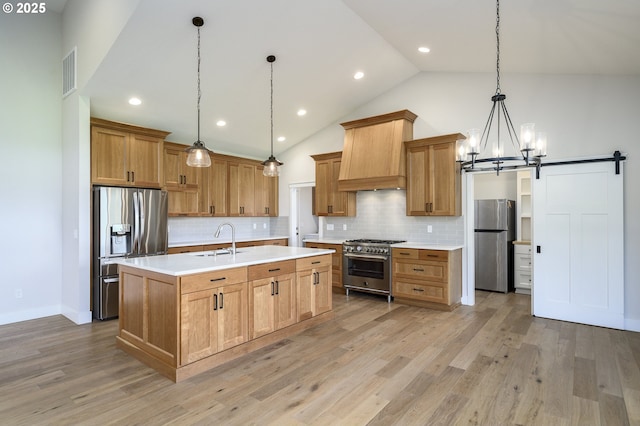 kitchen featuring a center island with sink, appliances with stainless steel finishes, tasteful backsplash, pendant lighting, and light hardwood / wood-style flooring