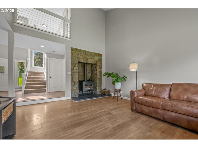 living area with stairs, a towering ceiling, a wood stove, and light wood-style floors