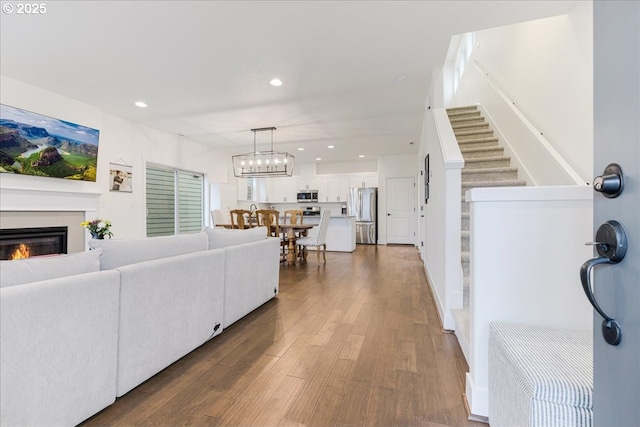 living area featuring stairs, a glass covered fireplace, recessed lighting, wood finished floors, and a notable chandelier