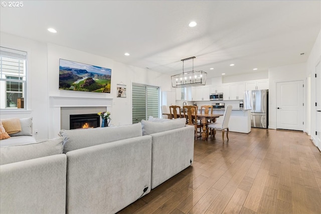 living area featuring recessed lighting, wood finished floors, a warm lit fireplace, and a chandelier