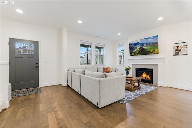 living room with a glass covered fireplace, recessed lighting, wood finished floors, and baseboards