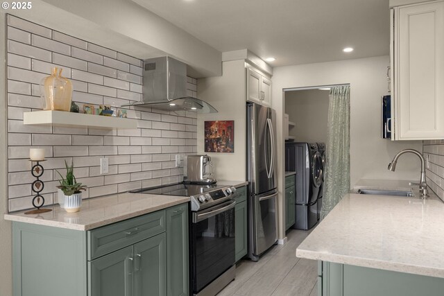 kitchen featuring washer and dryer, stainless steel appliances, wall chimney exhaust hood, sink, and white cabinetry