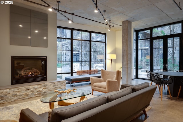 living room with french doors, plenty of natural light, a stone fireplace, and rail lighting