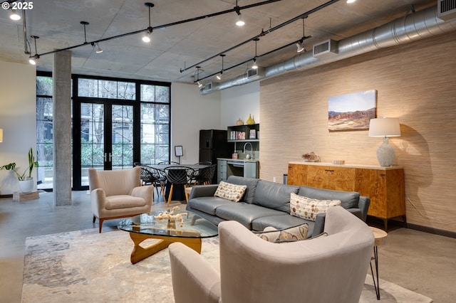 living room featuring french doors, concrete floors, rail lighting, baseboards, and a towering ceiling