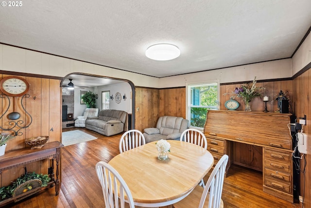 2720 Bowman Rd, Reedsport, OR 97467 - dining room featuring wood walls, hardwood / wood-style flooring, arched walkways, a textured ceiling, and a fireplace