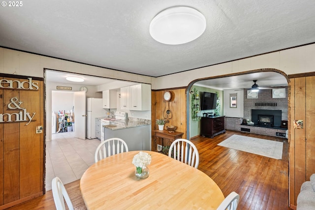 2720 Bowman Rd, Reedsport, OR 97467 - dining space featuring a ceiling fan, light wood-style flooring, a textured ceiling, a brick fireplace, and arched walkways