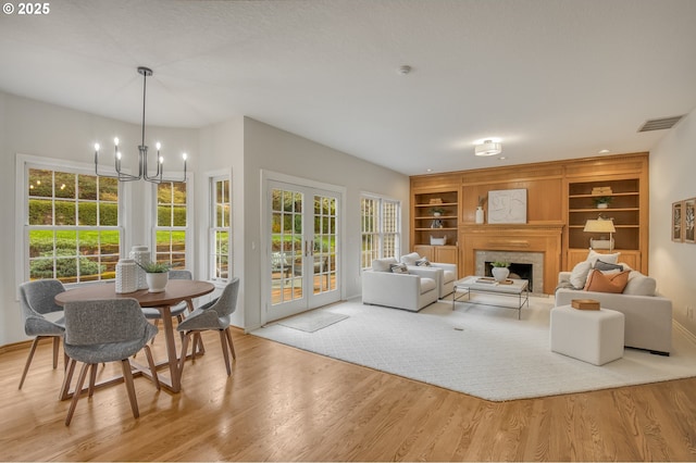 living room featuring a fireplace, a notable chandelier, wood finished floors, and french doors