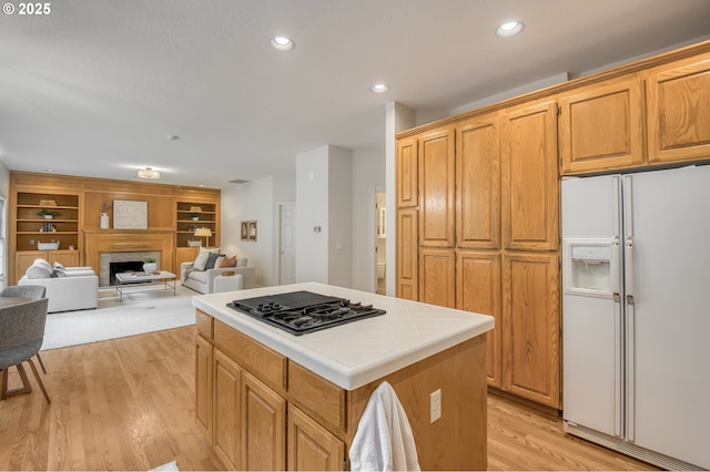 kitchen with light wood-type flooring, gas cooktop, a center island, white fridge with ice dispenser, and tile counters