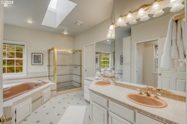 bathroom featuring double vanity, a skylight, a stall shower, a sink, and a bath