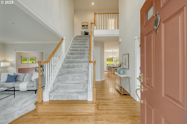 entryway with a wealth of natural light, stairway, light wood finished floors, and a towering ceiling