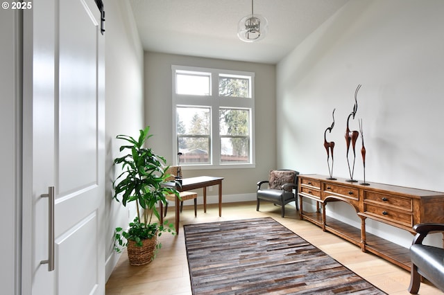 sitting room featuring a barn door, a textured ceiling, baseboards, and wood finished floors