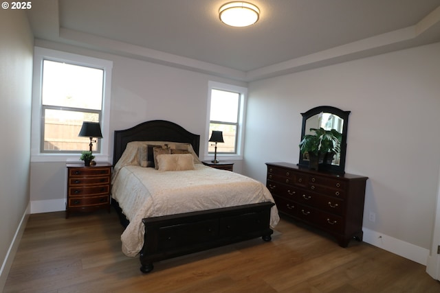 bedroom featuring a tray ceiling, wood finished floors, and baseboards