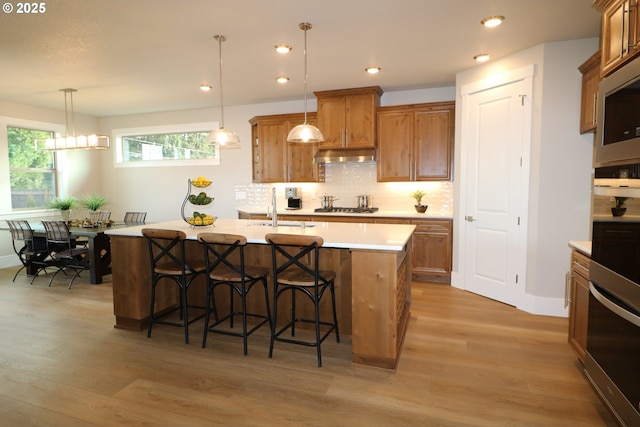 kitchen featuring brown cabinetry, appliances with stainless steel finishes, decorative light fixtures, light countertops, and a sink