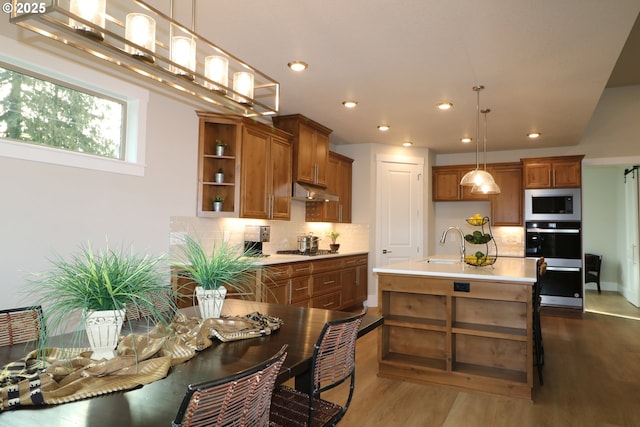 kitchen with an island with sink, stainless steel appliances, light countertops, and decorative light fixtures