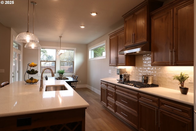 kitchen featuring decorative light fixtures, stainless steel gas cooktop, decorative backsplash, a sink, and under cabinet range hood