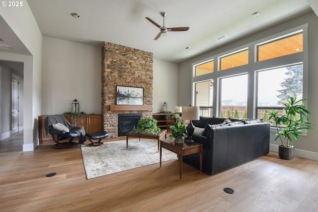 living room featuring a fireplace, visible vents, a textured ceiling, light wood-type flooring, and baseboards