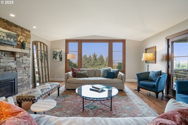 living room with hardwood / wood-style floors, a stone fireplace, and vaulted ceiling