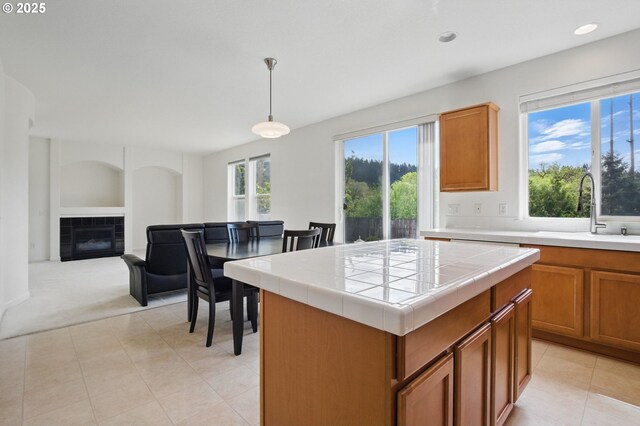 15820 SW Towhee Ln, Beaverton, OR 97007 - kitchen featuring tile countertops, a sink, brown cabinets, a tile fireplace, and hanging light fixtures