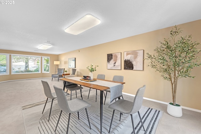 dining area featuring light colored carpet, baseboards, and a textured ceiling