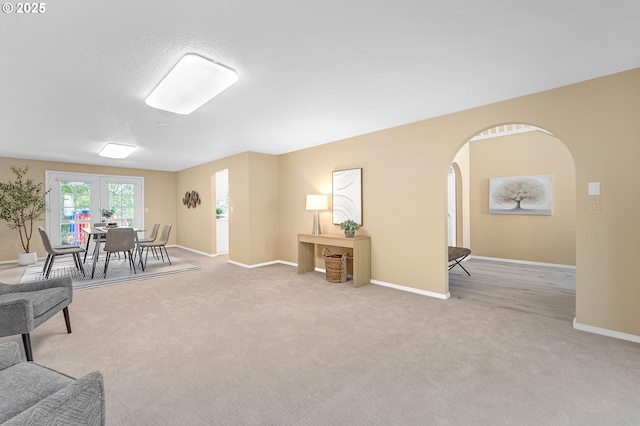 living area featuring arched walkways, carpet floors, baseboards, and a textured ceiling