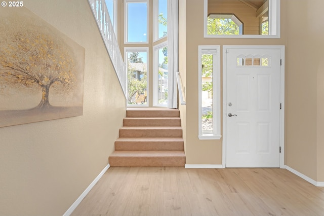 entryway with baseboards, wood finished floors, a towering ceiling, and stairs