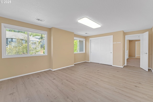 unfurnished bedroom with light wood-type flooring, baseboards, a textured ceiling, and a closet