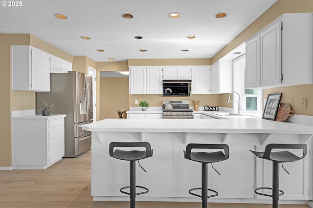 kitchen with appliances with stainless steel finishes, a sink, a peninsula, light wood-style floors, and white cabinets