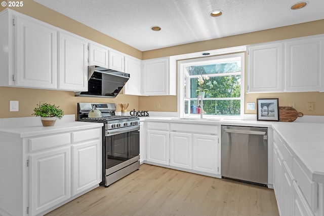 kitchen with appliances with stainless steel finishes, a sink, light wood-style floors, white cabinets, and a textured ceiling
