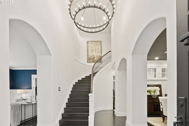 entrance foyer featuring arched walkways, a high ceiling, stairs, a chandelier, and baseboards