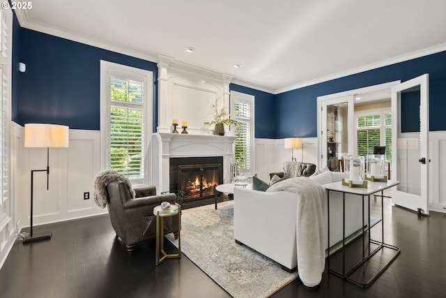 living area with a decorative wall, wainscoting, ornamental molding, a glass covered fireplace, and plenty of natural light