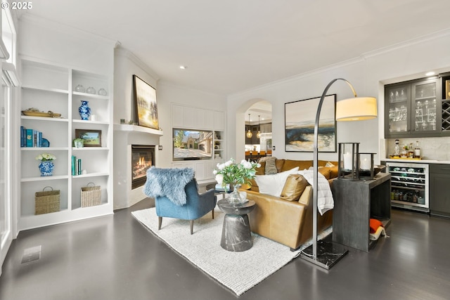living area with beverage cooler, a bar, ornamental molding, a glass covered fireplace, and arched walkways