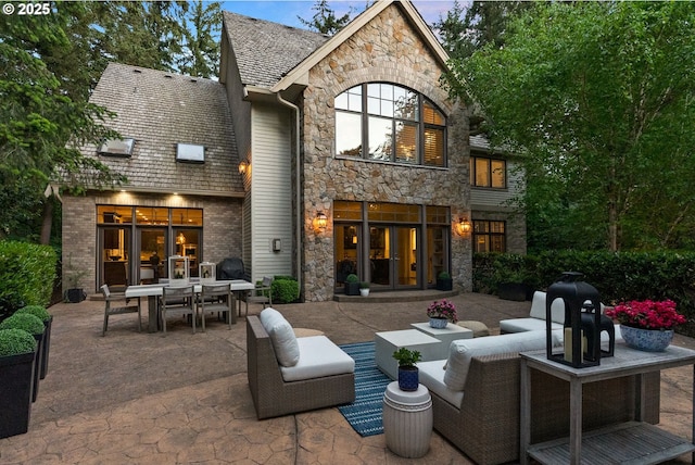 rear view of house with stone siding, a patio, french doors, and outdoor dining space