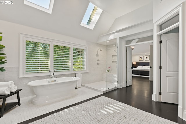 ensuite bathroom with a skylight, a shower stall, lofted ceiling, a freestanding bath, and wood finished floors