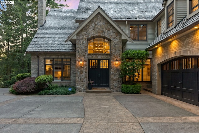 property entrance with stone siding, a chimney, asphalt driveway, and an attached garage