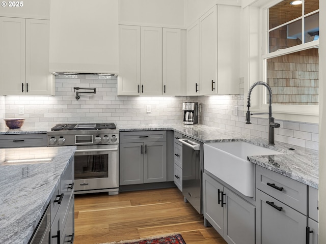 kitchen with sink, appliances with stainless steel finishes, gray cabinetry, light hardwood / wood-style floors, and light stone countertops