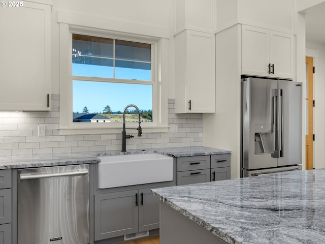 kitchen with sink, gray cabinetry, light stone counters, appliances with stainless steel finishes, and backsplash