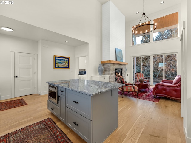 kitchen with light wood-type flooring, stainless steel microwave, pendant lighting, a fireplace, and light stone countertops