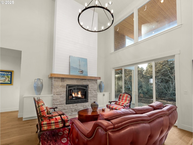 living room featuring a fireplace, a chandelier, light hardwood / wood-style flooring, and a high ceiling