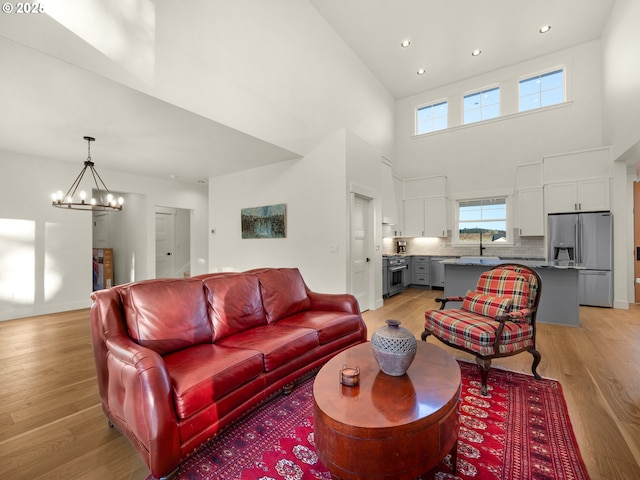 living room with sink, a notable chandelier, light hardwood / wood-style floors, and a towering ceiling