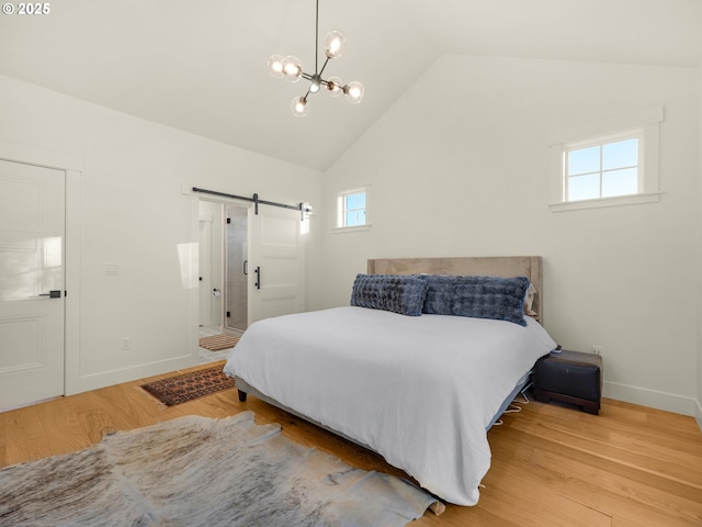 bedroom with vaulted ceiling, a barn door, hardwood / wood-style floors, and a chandelier