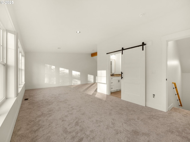 empty room featuring vaulted ceiling, light colored carpet, and a barn door