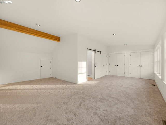 interior space with a barn door and vaulted ceiling with beams