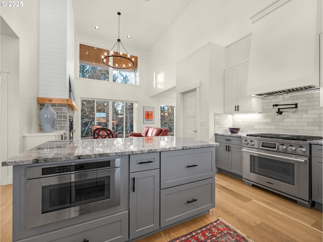 kitchen featuring custom exhaust hood, gray cabinets, pendant lighting, high end stove, and white cabinets