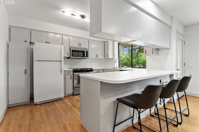 13980 Shireva Ct, Lake Oswego, OR 97034 - kitchen featuring stainless steel appliances, a peninsula, backsplash, light wood-type flooring, and light countertops