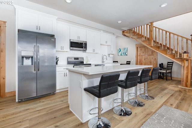 kitchen with light wood finished floors, appliances with stainless steel finishes, a kitchen island, and white cabinetry