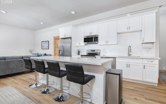 kitchen featuring light wood-style flooring, appliances with stainless steel finishes, open floor plan, white cabinetry, and a sink