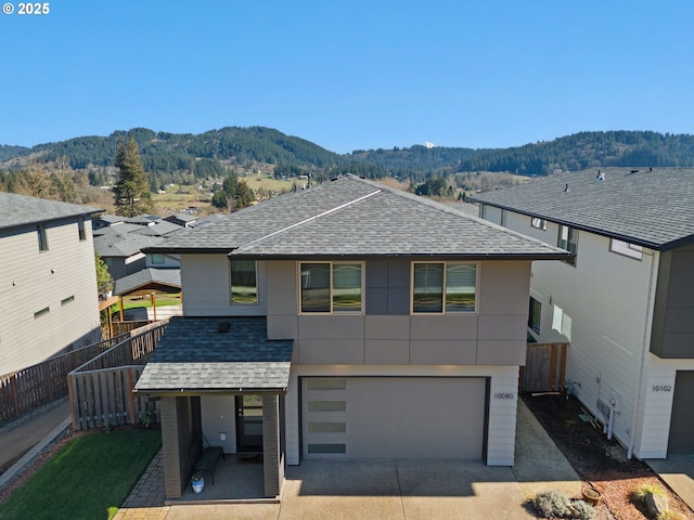 view of front of property featuring a shingled roof, an attached garage, fence, a mountain view, and driveway