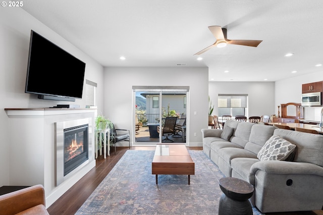 living area with ceiling fan, recessed lighting, baseboards, dark wood-style floors, and a glass covered fireplace