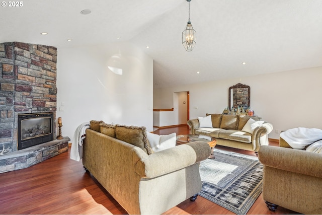 living room with vaulted ceiling, a stone fireplace, and wood finished floors