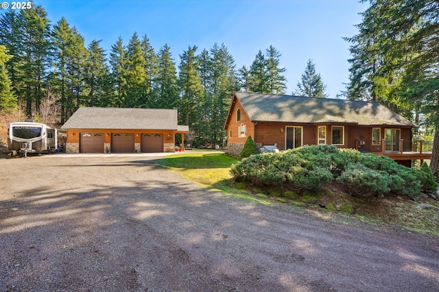 chalet / cabin with stone siding, an outbuilding, driveway, and a detached garage